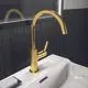 Goldene Waschtischarmatur von Ideal Standard mit hohem, gebogenem Auslauf und seitlichem Hebel, installiert auf einem weißen Waschbecken vor dunkler Wandfliesen.